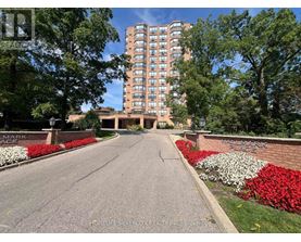 A tall building with many windows is surrounded by trees and a brick wall with the words "Fairmark Place" on it.
