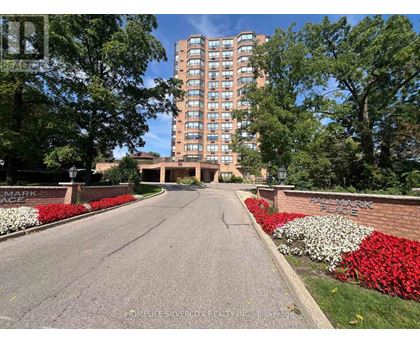 A tall building with many windows is surrounded by trees and a brick wall with the words "Fairmark Place" on it.