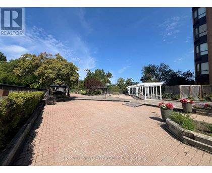 A brick pathway leads to a white gazebo in a sunny garden.
