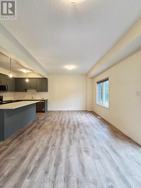 A spacious room with wooden flooring and a window on the right side.