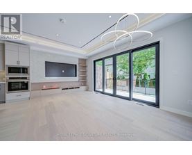 A spacious, well-lit living room with a television, built-in cabinets, and a large window.