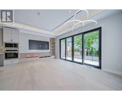 A spacious, well-lit living room with a television, built-in cabinets, and a large window.