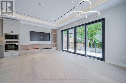 A spacious, well-lit living room with a television, built-in cabinets, and a large window.