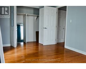 A room with wooden floors and white walls, with a door on the left and two doors on the right.