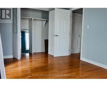 A room with wooden floors and white walls, with a door on the left and two doors on the right.