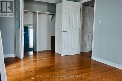 A room with wooden floors and white walls, with a door on the left and two doors on the right.
