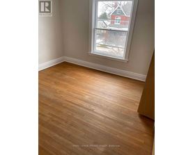 A room with wooden flooring and a window showing a view of a red house.