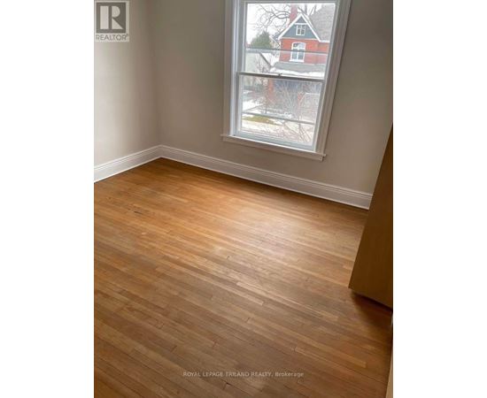 A room with wooden flooring and a window showing a view of a red house.