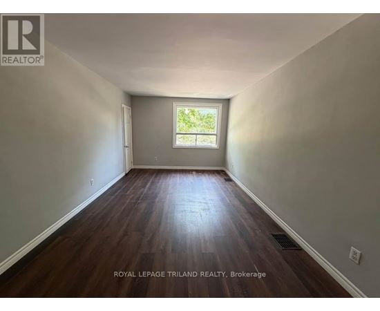 A room with wooden floors and a window showing greenery outside.