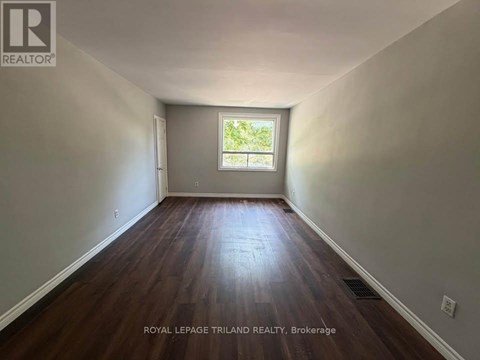 A room with wooden floors and a window showing greenery outside.