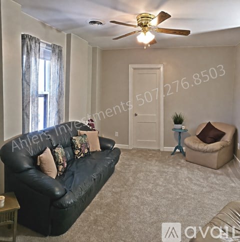 A living room with a black leather couch and a ceiling fan.