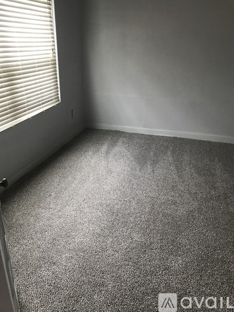 A room with a carpeted floor and a window with blinds.