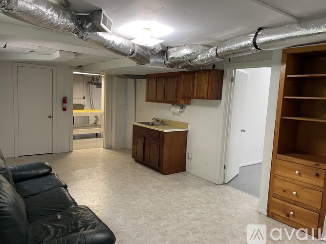 A living room with a black leather couch and a kitchenette in the background.