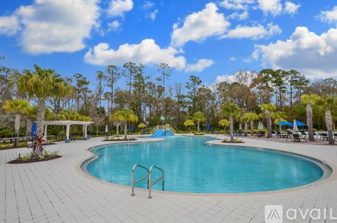 A large outdoor swimming pool surrounded by trees and a clear blue sky.