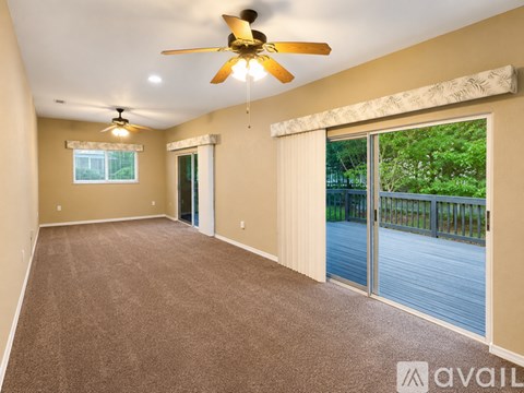 A spacious room with a ceiling fan and sliding glass doors leading to a deck.