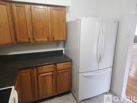 A white refrigerator stands in a kitchen with wooden cabinets.