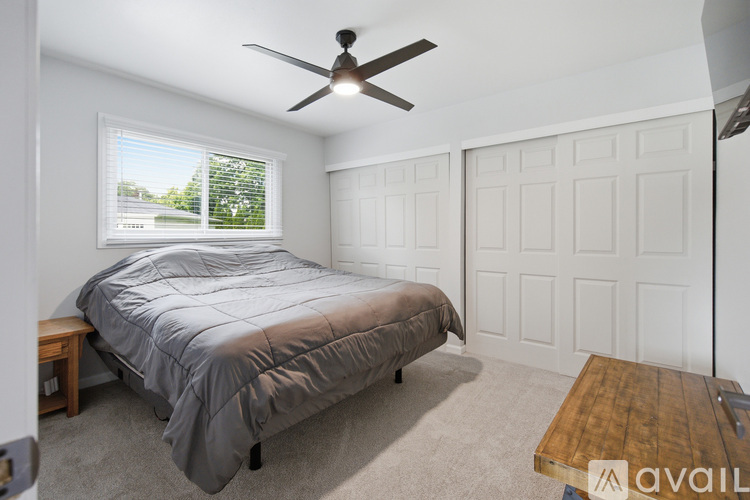 A bedroom with a bed, a ceiling fan, and a window with a view of the outside.