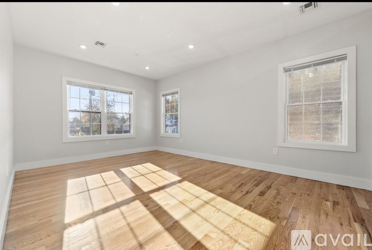 A spacious room with wooden flooring and two windows.
