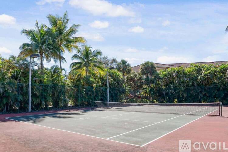 A tennis court surrounded by palm trees and a fence.