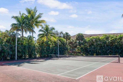 A tennis court surrounded by palm trees and a fence.