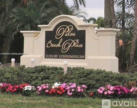A sign for Palm Beach Place, a luxury condominium, is displayed in front of some flowers.
