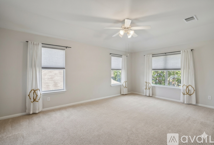 A spacious room with a ceiling fan and three windows.