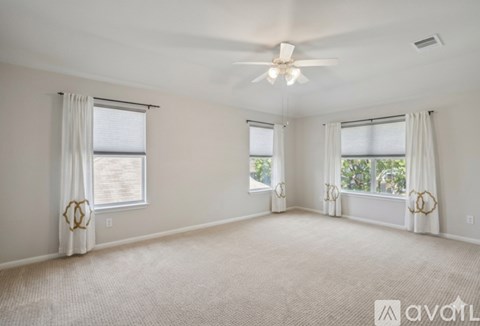 A spacious room with a ceiling fan and three windows.