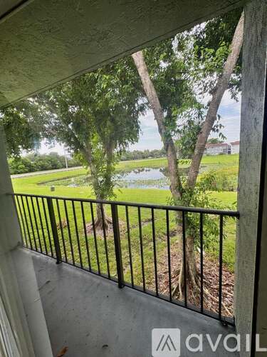 A balcony with a metal railing overlooks a grassy area with trees and a body of water.