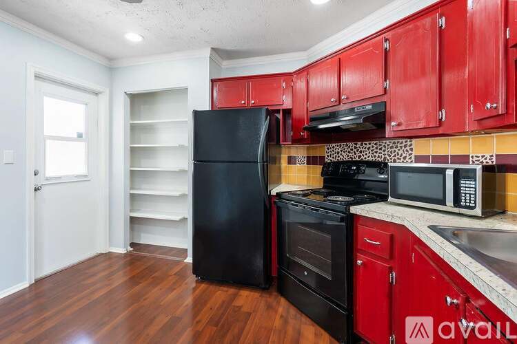 A kitchen with red cabinets and black appliances.