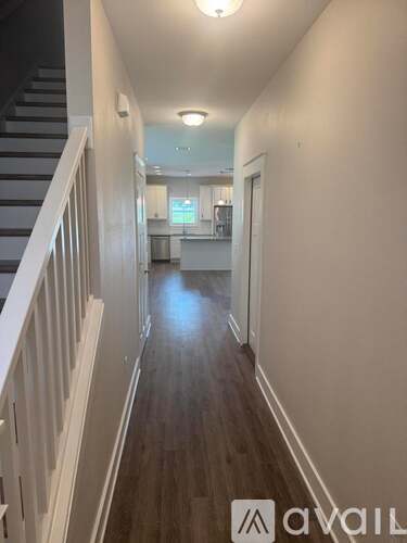 A long hallway with a staircase on the left and a kitchen area in the distance.