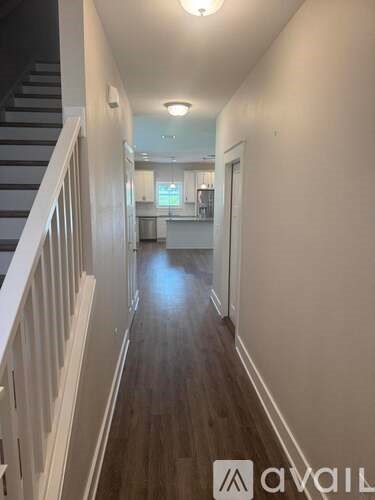 A long hallway with a staircase on the left and a kitchen area in the distance.