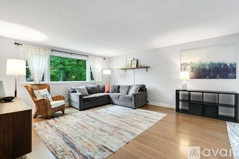 A living room with a grey couch, a brown chair, a rug and a painting on the wall.