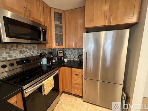 A kitchen with a stainless steel refrigerator, black stove, and wooden cabinets.