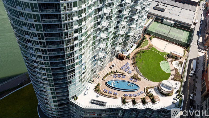 A tall glass building with a pool and a green lawn in front.