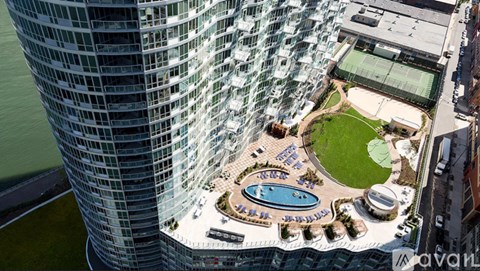 A tall glass building with a pool and a green lawn in front.