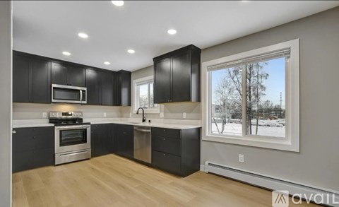 A kitchen with black cabinets and a window showing a snowy landscape outside.