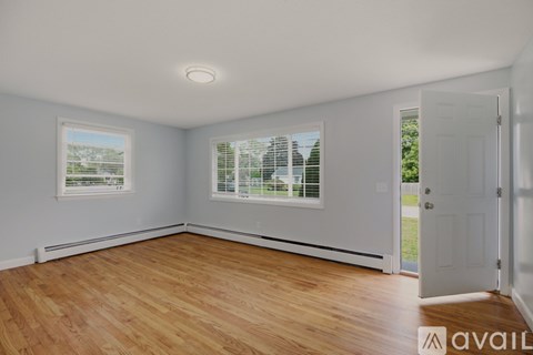 A room with wooden floors and white walls, with a window showing a view of a fence and trees.