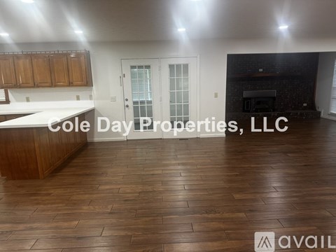 A spacious room with wooden flooring and a kitchen area with cabinets and a countertop.