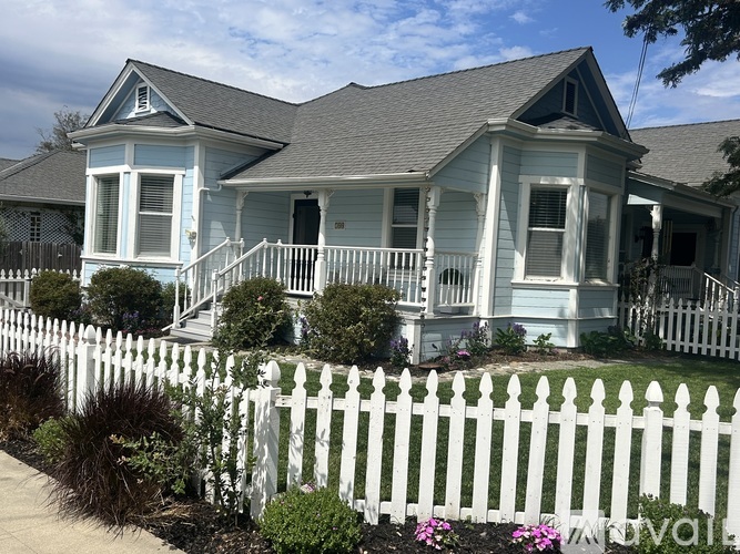 A white picket fence surrounds a two-story house with a blue front.