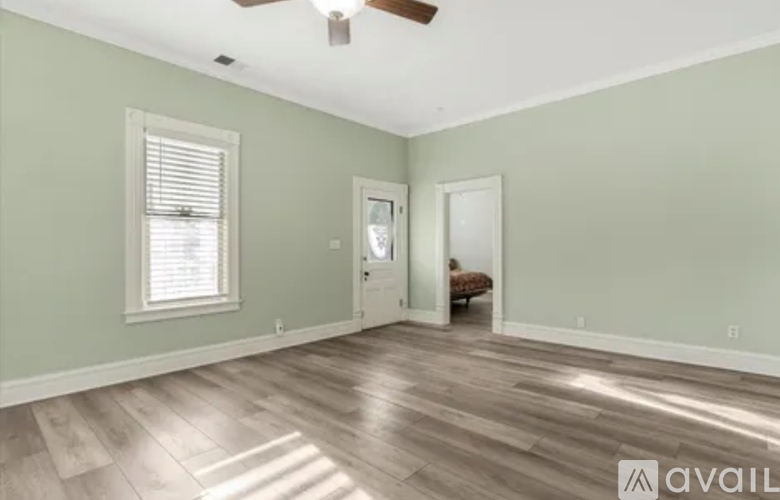 A room with a ceiling fan and light, a window with blinds, and a door leading to another room.
