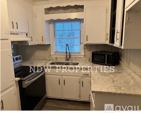 A kitchen with white cabinets and a window with blinds.