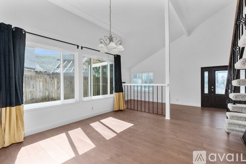 A spacious room with wooden flooring and a staircase on the right side.