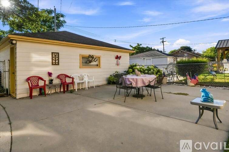 A small white building with a yellow door and a sign that reads "available" is surrounded by a patio with red chairs and a table.