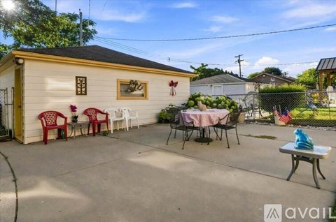 A small white building with a yellow door and a sign that reads "available" is surrounded by a patio with red chairs and a table.