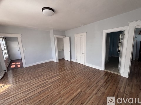 A room with wooden floors and white walls, with a door on the left and a door on the right.