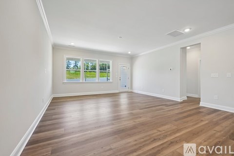 A spacious room with wooden flooring and a large window overlooking a green landscape.