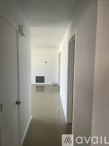 A hallway with a door on the left and a desk with a laptop on it in the distance.