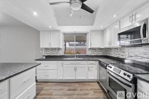 A kitchen with white cabinets and black countertops.