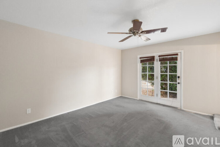 A room with a ceiling fan and a window with a view of trees.