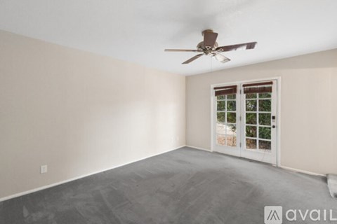 A room with a ceiling fan and a window with a view of trees.